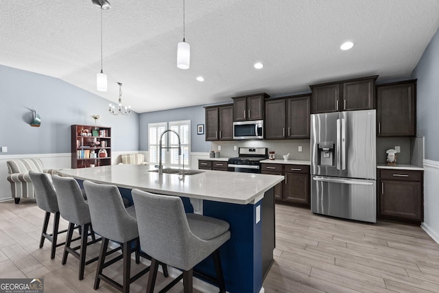 kitchen with appliances with stainless steel finishes, a breakfast bar, light countertops, dark brown cabinets, and a sink