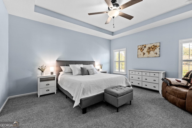 bedroom with carpet floors, a tray ceiling, multiple windows, and baseboards