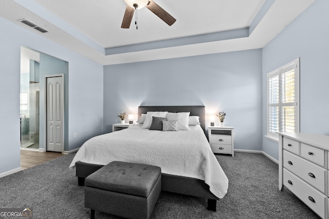 bedroom featuring dark carpet, a raised ceiling, visible vents, and baseboards