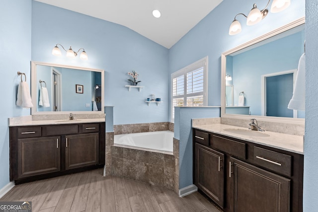 bathroom featuring two vanities, vaulted ceiling, a sink, wood finished floors, and a bath