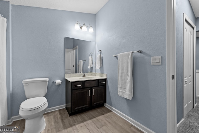 bathroom featuring baseboards, vanity, toilet, and wood finished floors