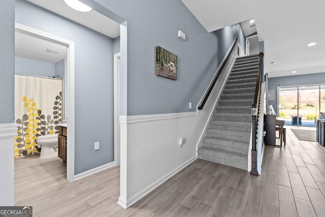 stairs with wainscoting, wood finished floors, and baseboards