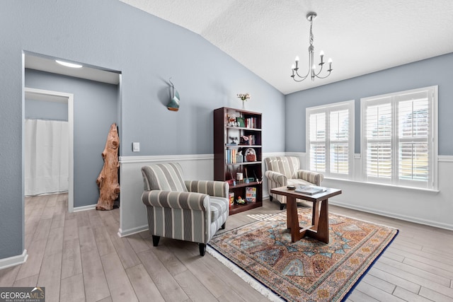 living area featuring lofted ceiling, a textured ceiling, a notable chandelier, wood finished floors, and baseboards