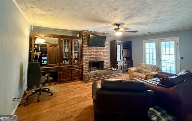 living area featuring light wood-style flooring, ceiling fan, a textured ceiling, french doors, and a brick fireplace