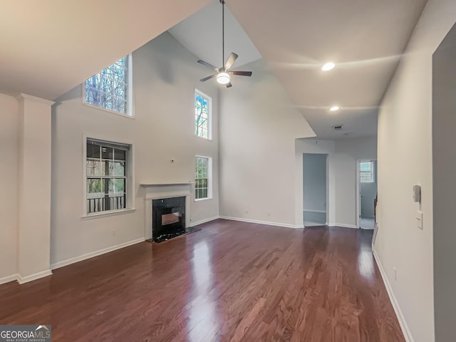 unfurnished living room with baseboards, dark wood finished floors, a ceiling fan, a towering ceiling, and a high end fireplace