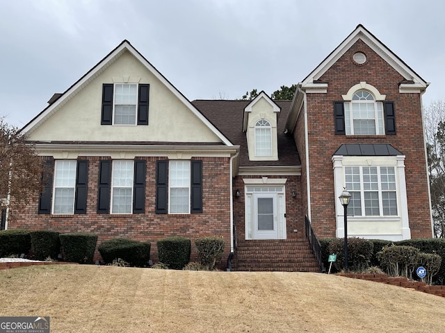 traditional-style home featuring entry steps, brick siding, a front lawn, and stucco siding