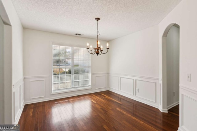 unfurnished dining area featuring a textured ceiling, arched walkways, dark wood finished floors, and an inviting chandelier