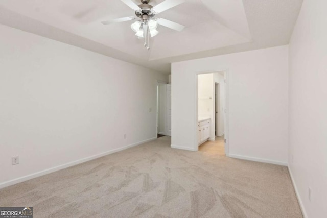 unfurnished bedroom featuring light carpet, baseboards, a tray ceiling, and ensuite bathroom