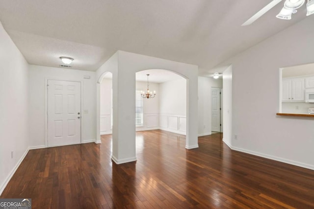 interior space with dark wood-style floors, ceiling fan with notable chandelier, arched walkways, and baseboards