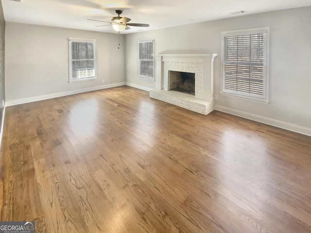 unfurnished living room with a wealth of natural light, wood finished floors, a fireplace, and ceiling fan