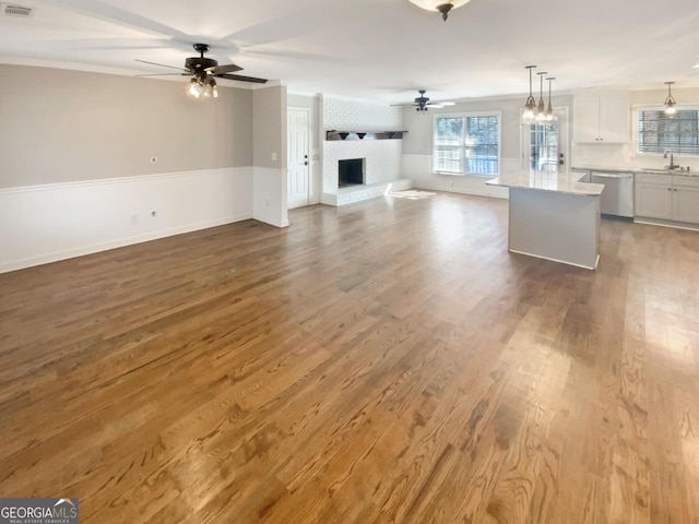 unfurnished living room with a ceiling fan, a brick fireplace, a sink, and wood finished floors