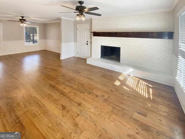 unfurnished living room featuring brick wall, wood finished floors, a ceiling fan, a brick fireplace, and crown molding