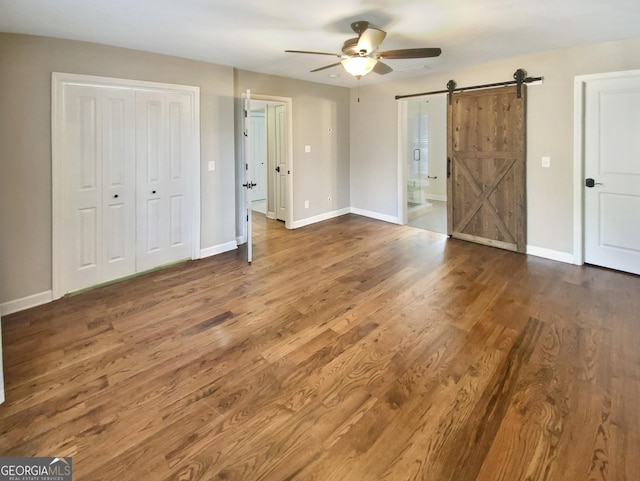 unfurnished bedroom featuring a barn door, connected bathroom, ceiling fan, wood finished floors, and baseboards