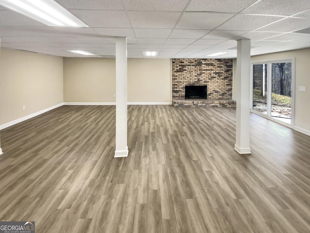 basement featuring a paneled ceiling, a fireplace, baseboards, and wood finished floors