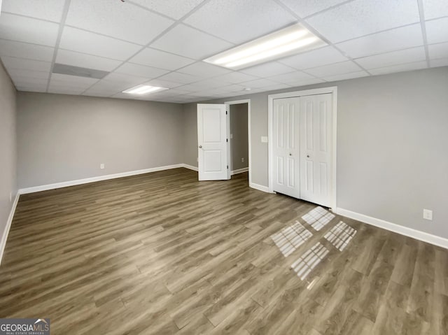 finished below grade area featuring a drop ceiling, baseboards, and wood finished floors