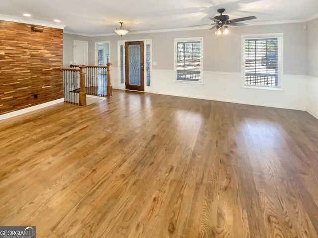 unfurnished living room featuring ornamental molding, wood walls, ceiling fan, and wood finished floors