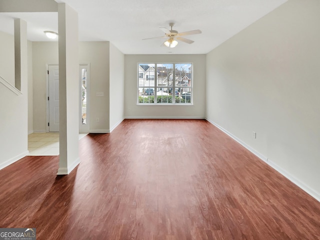 unfurnished living room featuring baseboards, a ceiling fan, and dark wood-style flooring