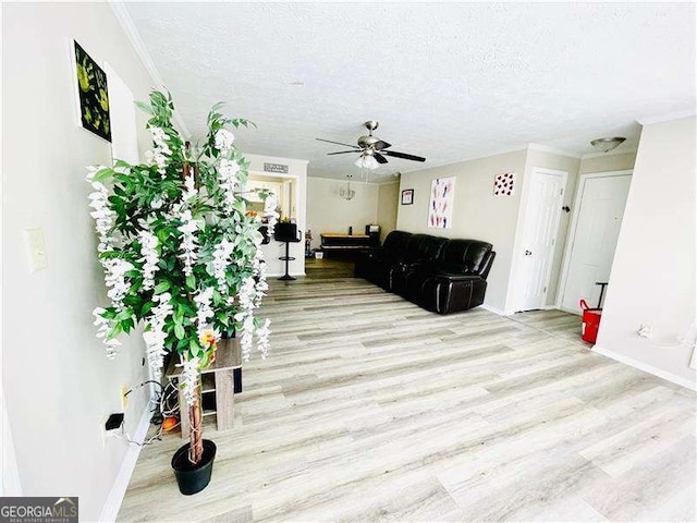 living area featuring light wood-type flooring, ceiling fan, a textured ceiling, and baseboards