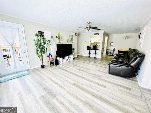 living room featuring a textured ceiling, ceiling fan with notable chandelier, light wood-style flooring, and baseboards