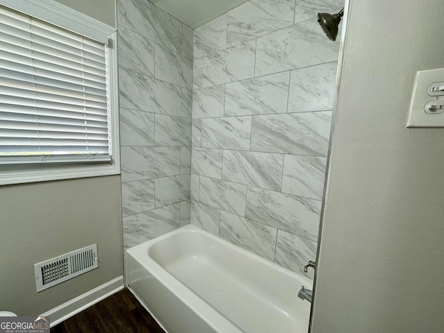 bathroom featuring wood finished floors, bathtub / shower combination, visible vents, and baseboards