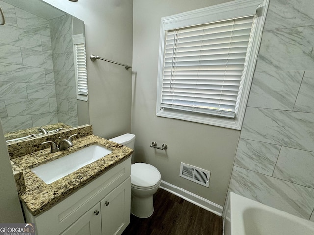 bathroom with visible vents, toilet, a tub, wood finished floors, and vanity