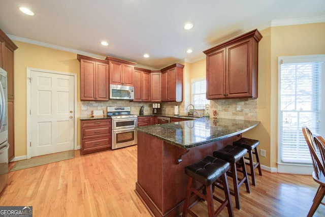 kitchen featuring decorative backsplash, ornamental molding, a breakfast bar, a peninsula, and stainless steel appliances