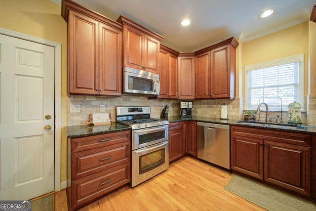 kitchen with appliances with stainless steel finishes, light wood-type flooring, a sink, and decorative backsplash