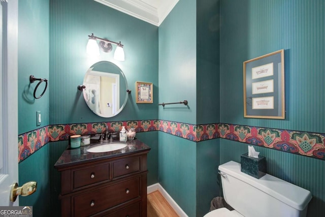 bathroom with toilet, wallpapered walls, ornamental molding, and vanity