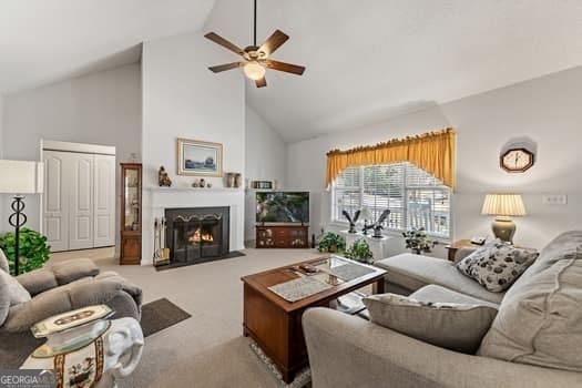 carpeted living room featuring high vaulted ceiling, ceiling fan, and a lit fireplace