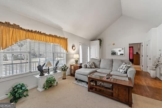 carpeted living area with high vaulted ceiling and baseboards