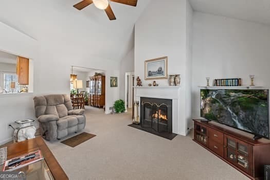 carpeted living area with a fireplace with flush hearth, high vaulted ceiling, and a ceiling fan