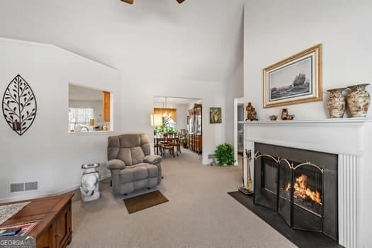 interior space with carpet floors, a warm lit fireplace, visible vents, and high vaulted ceiling