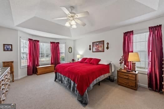 bedroom featuring light carpet, baseboards, a tray ceiling, and a ceiling fan