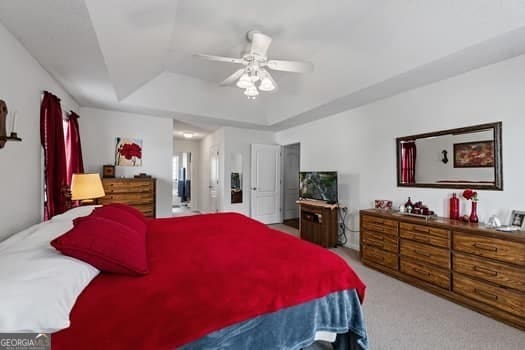 carpeted bedroom with a tray ceiling and a ceiling fan