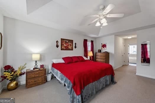 carpeted bedroom featuring a raised ceiling, ceiling fan, and baseboards