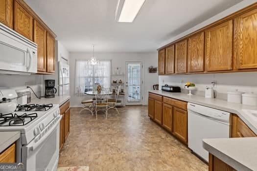 kitchen featuring brown cabinets, white appliances, light countertops, and hanging light fixtures