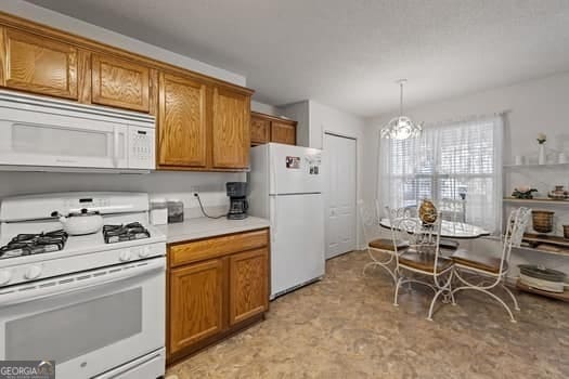 kitchen featuring light countertops, white appliances, brown cabinetry, and pendant lighting