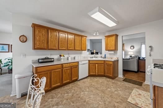 kitchen featuring range with gas cooktop, light countertops, brown cabinetry, white dishwasher, and a sink