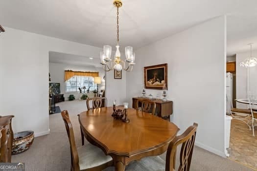 dining room featuring baseboards, a notable chandelier, and light colored carpet