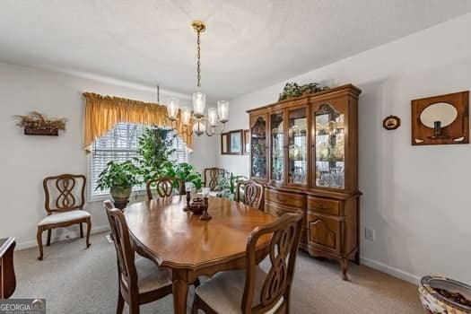 dining room featuring a chandelier, light colored carpet, and baseboards