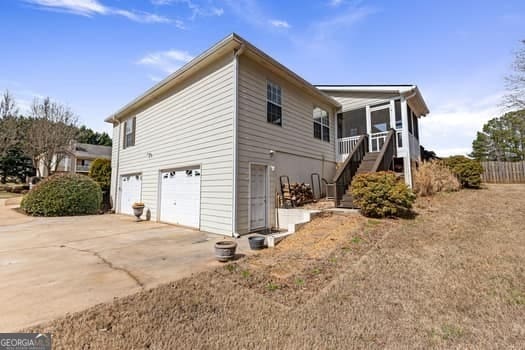 view of home's exterior featuring concrete driveway, stairway, an attached garage, a sunroom, and fence