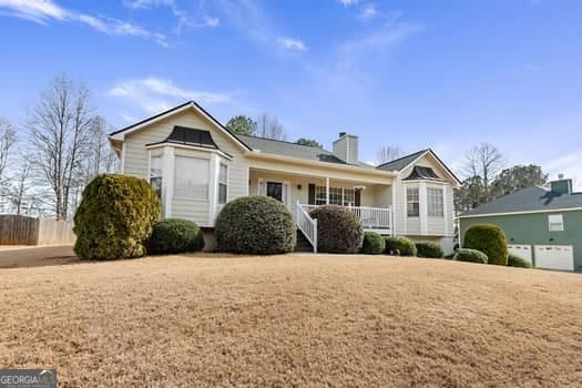 ranch-style house with covered porch, fence, and a chimney