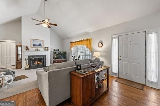 living area featuring a lit fireplace, high vaulted ceiling, and dark wood-type flooring