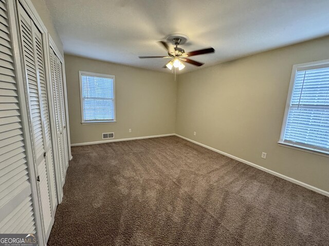 2430 Fern Valley Ct, East Point, GA 30344 - unfurnished bedroom featuring multiple windows, dark colored carpet, two closets, and a ceiling fan