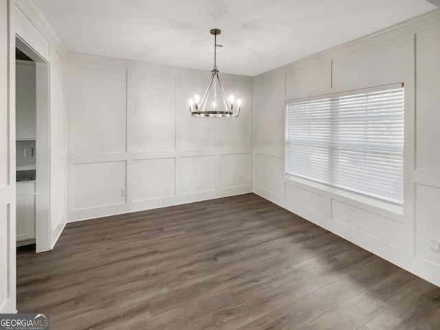 unfurnished dining area with dark wood-style flooring, a notable chandelier, and a decorative wall