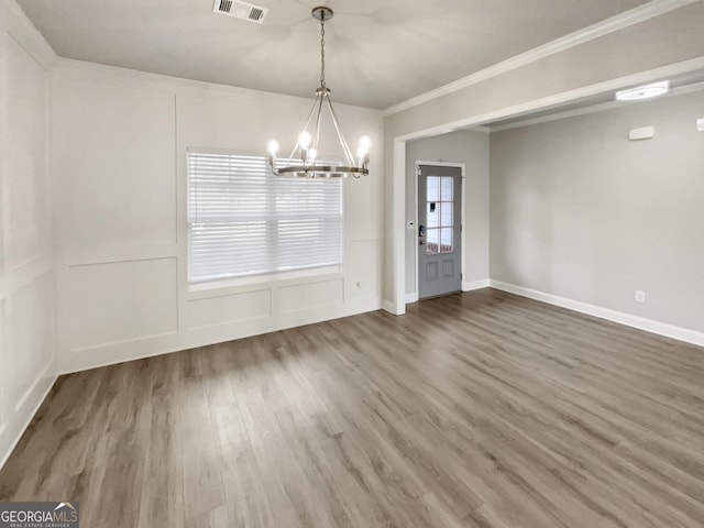 unfurnished dining area with visible vents, wood finished floors, an inviting chandelier, crown molding, and a decorative wall