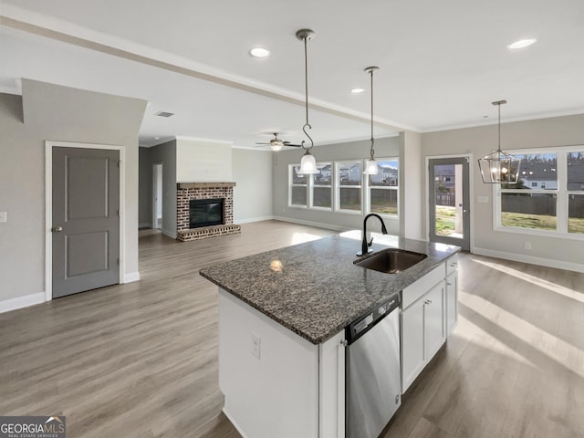 kitchen with a brick fireplace, white cabinetry, a sink, wood finished floors, and dishwasher