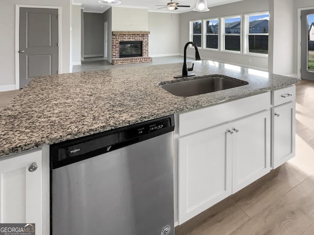 kitchen featuring stone counters, a fireplace, a sink, open floor plan, and stainless steel dishwasher