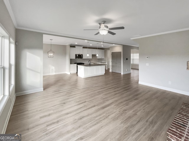 unfurnished living room with ornamental molding, a healthy amount of sunlight, ceiling fan, wood finished floors, and baseboards