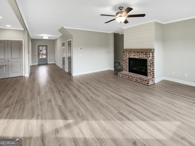 unfurnished living room featuring a fireplace, crown molding, baseboards, and wood finished floors